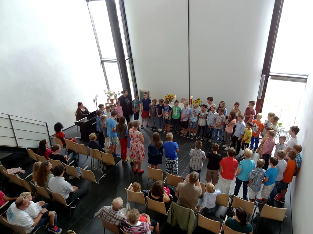 Schülergruppe steht singend vor der Bestuhlung in der Kirche.